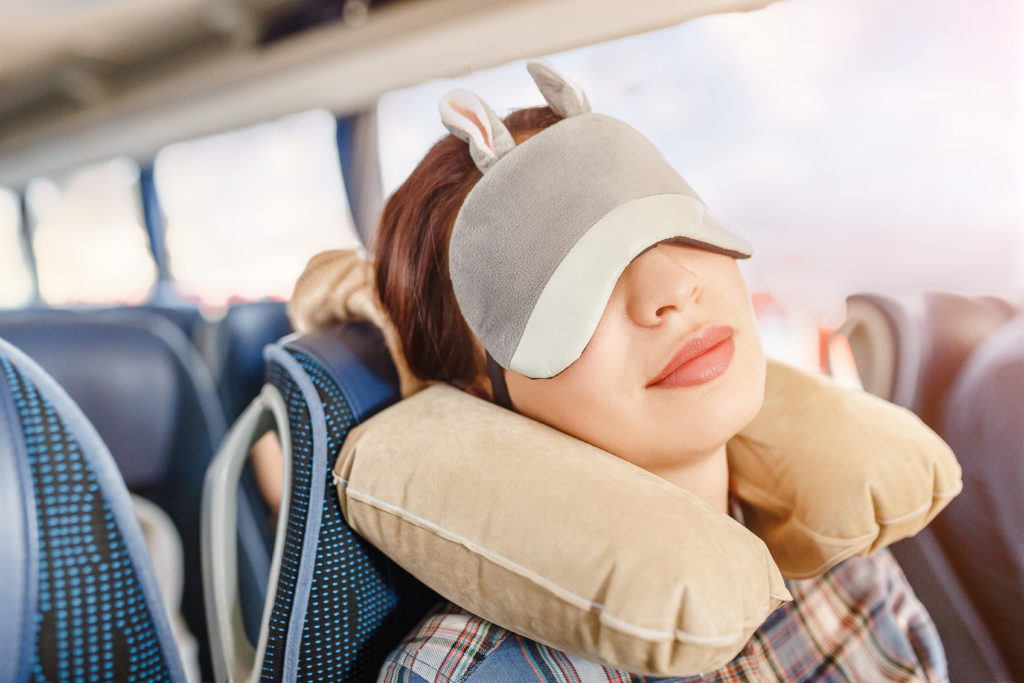 woman sleeping on bus rides wearing an eye mask and a neck pillow